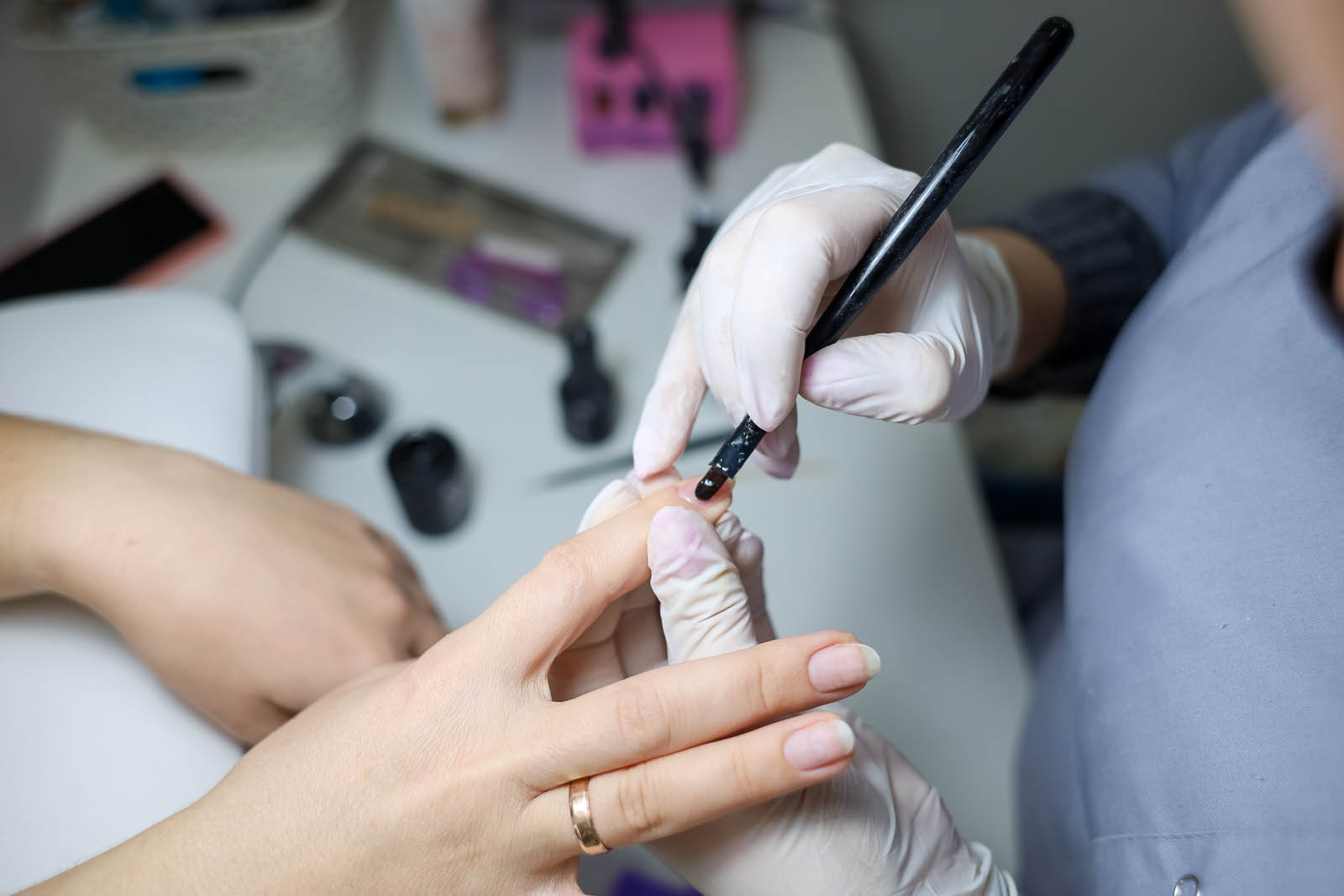 The manicurist applies gel polish to the client's nails. The manicure master works with a brush and nail polish